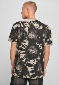 Sort med beige tie-dye kortermet t-skjorte med rund hals og løs passform, i et strukturert stoff med abstrakte mønstre.