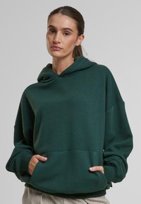 Mørkegrøn hoodie med en kængurulomme, brede ærmer og hætte med snoretræk. Blødt, glat stof i en afslappet pasform.