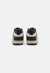 Sneakers in pelle marrone scuro con dettagli bianchi. Tallone rotondo, superficie texturizzata e suola beige chiaro. Design minimalista senza branding visibile.
