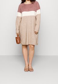 Knit dress featuring color blocks in burgundy, cream, and taupe, with long sleeves and a loose fit. Complemented by a brown handbag.