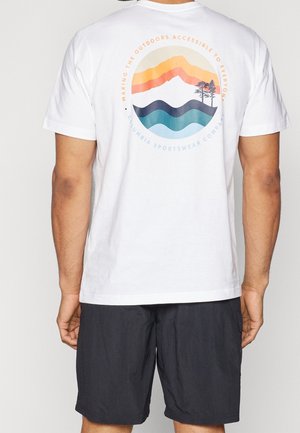 Mann trägt weißes T-Shirt mit farbigem Berg- und Wellen-Design und Text "Making the outdoors accessible to everyone" auf dem Rücken.