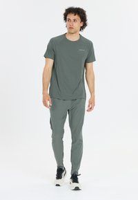 Lyhythihainen urheilupaita ja tapered-housut hillityssä vihreässä, valmistettu kevyistä materiaaleista. Mustat lenkkarit täydentävät asua.