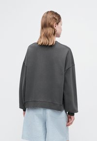 Sudadera gris de gran tamaño con hombros caídos, puños acanalados y un dobladillo curvado. Combinada con pantalones cortos de textura azul claro.