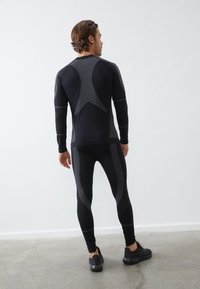 Svart idrottstop och leggings med en strukturerad mönster och kontrasterande ränder. Designad för en åtsittande silhuett med en mjuk textur.