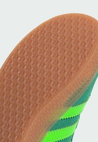 Gummisulor i orange med ett texturerat mönster av små stjärnor. Ovandelen har grönt tyg med djärva svarta ränder.