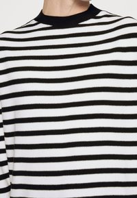 Svetr pletený černobílými pruhy s kulatým výstřihem. Má střídavé široké a úzké pruhy, měkkou texturu a elastické manžety.