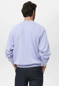 Felpa crewneck lilla con vestibilità rilassata, polsini a costine e texture morbida, abbinata a pantaloni scuri e affusolati.
