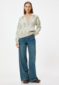 Strickpullover in Creme mit Rautenmuster, mit einem Kragenhalsausschnitt und geripptem Saum, kombiniert mit weiten blauen Jeans.