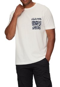 Witte katoen t-shirt met een marineblauwe zak waarin "PARADISE" in vetgedrukte letters is afgedrukt. Korte mouwen en een ontspannen pasvorm met een minimale textuur.