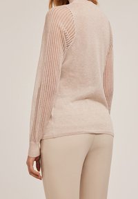 Pull rose clair avec manches côtelées verticales et texture lisse et douce. Doté d'un col haut et associé à un pantalon beige.