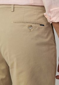 Khakifarbene Baumwollhose mit einer Gesäßtasche, die mit einem Knopfverschluss und einem kleinen Logotag versehen ist. Angenehme Textur und taillierte Passform.