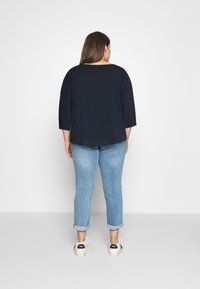 Maglietta navy a tre quarti abbinata a jeans azzurri con risvolto e sneakers bianche con dettagli neri. Outfit semplice e informale.