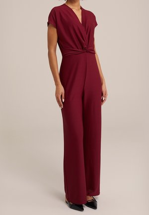 Bordeauxroter Jumpsuit mit kurzen Ärmeln, gedrehtem Vorderteil, weiten Beinen und glatter Textur; kombiniert mit schwarzen spitzen Ballerinas.