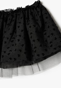 Gonna nera a strati realizzata in tessuto strutturato con un sovraccoperta di tulle trasparente. Presenta una vita arricciata e motivi floreali su tutta la superficie.