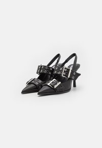 Črne slingback pete s špičastimi prsti, opremljene s širokimi trakovi in srebrno kovinsko opremo ter grometi, na vitkem petnem delu. Gladek usnjen videz.