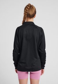 Top nero a maniche lunghe con tessuto testurizzato e colletto, abbinato a pantaloni corti aderenti rosa. Il top presenta strisce in evidenza sulle maniche.