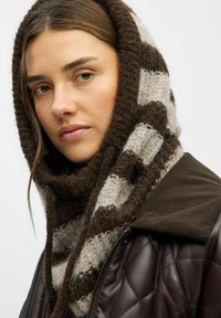 Brun og creme stribet strikscarf med en blød tekstur, båret med en brun quiltet jakke med en ribbet krave.