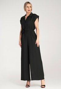 Czarny kombinezon z kołnierzykiem, krótkimi rękawami i szerokimi nogawkami. Posiada marszczony detal w talii z kwiatowym akcentem.