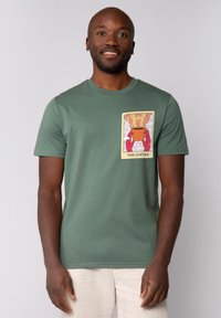Groen katoenen T-shirt met een grafisch ontwerp van een rode en oranje koffiekop in een geïllustreerde stijl, gepresenteerd in een ontspannen pasvorm.