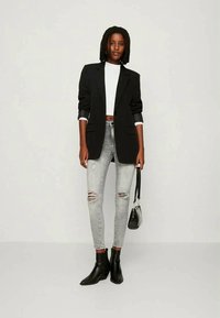 Juodas bleizeris, baltas marškinėlis, pilki suplėšyti džinsai ir juodi kulkšnies batai. Priedai apima mažą juodą rankinę. Paprasti dizaino elementai visur.