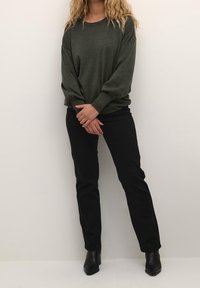 Maglione verde oliva scuro a maniche lunghe, vestibilità rilassata; abbinato a pantaloni neri aderenti e stivali neri a punta con tacco.