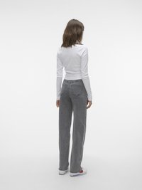 Haut blanc à manches longues associé à un jean gris taille haute et évasé. Le jean présente des rayures verticales discrètes et des poches arrière.