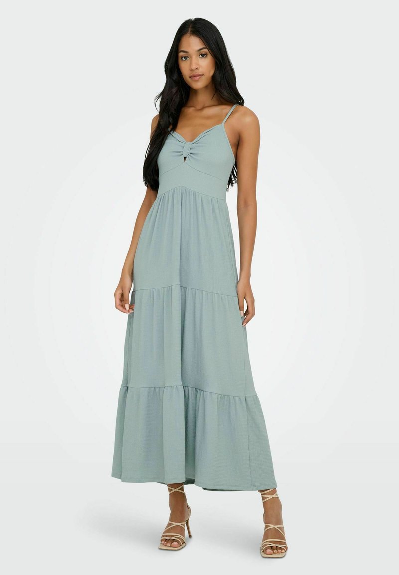 Robe maxi en tissu vert clair, présentant un corsage ajusté avec un détail en torsion et une ouverture en forme de clé, une jupe à volants et de fines bretelles.