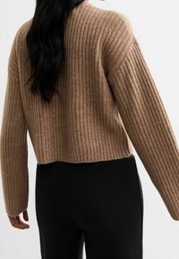 Pull court en tricot ribbé beige avec des manches longues et un col rond, associé à un pantalon noir ajusté.
