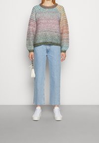 Maglione lavorato a maglia multicolore con strisce gradienti, scollatura rotonda e polsini a costine; abbinato a jeans dritti blu chiaro e sneaker bianche.