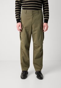 Cargo-Hosen in Olivgrün, aus leichtem Stoff, mit mehreren Seitentaschen und entspanntem Schnitt. Kombiniert mit schwarzen Schuhen.
