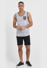 Hallikashallikas ja valge mustriga top tumeda halli rinnataskuga, kombineeritud mustade üleskeeratud lühikeste pükstega ja mustade tossudega.