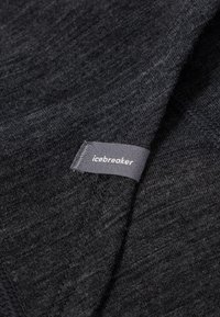 Tela gris oscuro con una apariencia texturada, que presenta una etiqueta con el logotipo "icebreaker" cosida en el borde. Apta para diversos artículos de ropa.
