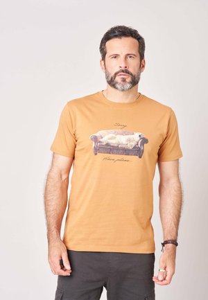 Man met baard draagt een oranje t-shirt met een afbeelding van een ijsbeer die op een bank ligt en tekst die "Sorry Have plans." leest