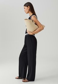 Pantaloni neri a gamba larga abbinati a un top nero senza maniche. La modella tiene una grande borsa tote di paglia beige con accenti neri.