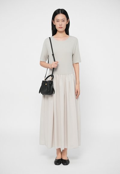 Jasnoszara bluzka z krótkim rękawem z zebraniem w talii, połączona z luźną kremową spódnicą. Trzyma małą czarną torebkę. Czarne baleriny.