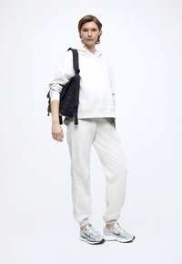 Ανοιχτό γκρι φούτερ με κουκούλα και τσέπη καγκουρό, αντίστοιχο παντελόνι φόρμας και ανοιχτά μπλε αθλητικά παπούτσια. Μαύρο σακίδιο πλάτης κρεμασμένο σε έναν ώμο.