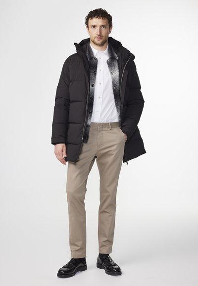 Svart puffjacka med huva, vit skjorta och beige byxor. Bärs med svarta loafers, med knappdetaljer och släta tygtexturer.