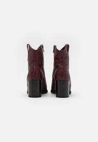 Bottes chelsea à imprimé serpent rouge avec une finition texturée, dotées d'un talon bloc noir et de fermetures éclair sur les côtés, présentant un design moderne.