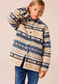 Polarowy jacket w geometryczne wzory w odcieniach beżu, niebieskiego i brązowego. Posiada napy i kołnierz typu spread, uzupełniony zwężanymi rękawami.