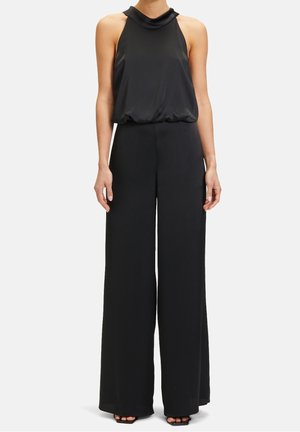Bezrekawowy czarny satynowy top na szyję zestawiony z wysokim stanem, szerokimi czarnymi spodniami oraz czarnymi sandałami na obcasie z odkrytymi palcami.