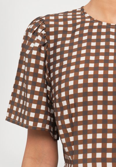 Blusa a cuadros marrones y blancos, con mangas cortas abullonadas, escote redondo y tejido suave con una textura lisa.