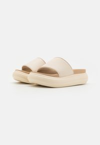 Béžové šľapky na slip-on s textúrovaným vrchom a otvorenou špičkou. Mäkko polstrovaný vnútorný výplň a masívna, tlmiaca podrážka. Minimálne značenie na boku.