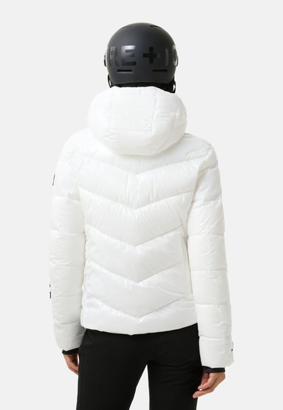 Witte pufferjack met chevront patroon, voorzien van een capuchon, gequilte textuur en zwarte accenten. G gedragen met zwarte broek en een zwarte helm.