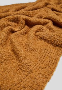 Tissu en laine douce et texturée de couleur moutarde avec des boucles et des plis visibles, créant une apparence chaleureuse et confortable.