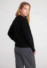 Suéter negro de punto con un ajuste relajado, dobladillo acanalado y mangas largas, combinado con pantalones de pierna ancha grises. Detalle de superficie texturizada visible.