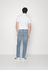 Jeans de denim ajustados de color azul claro con un desvanecimiento sutil, combinados con una camisa blanca de manga corta y zapatillas blancas. Diseño simple, look casual.