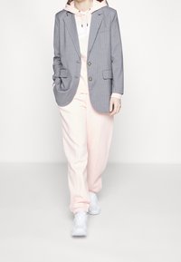 Grå randig kavaj över en rosa hoodie och matchande sweatpants, tillsammans med vita sneakers, med avslappnad passform och mjuka texturer.