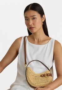 Pinuma salmu rokassoma ar pusmēness formu, kurai ir brūna ādas siksna un sprādze. Tekstūrēts materiāls, elegants dizains.