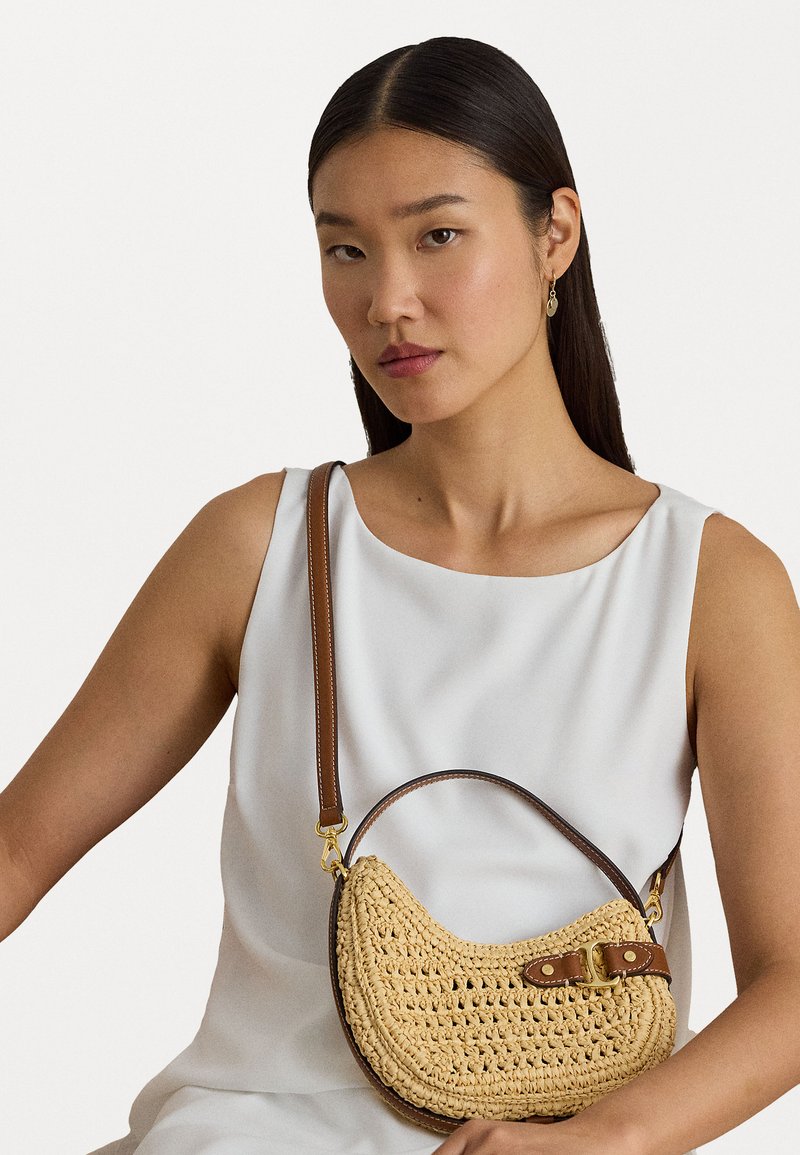 Pinuma salmu rokassoma ar pusmēness formu, kurai ir brūna ādas siksna un sprādze. Tekstūrēts materiāls, elegants dizains.