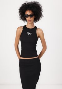 Svart ribbestrikket tanktop med rund hals og cropped design, prydet med en sølv CK-logo. Signert med en matchende svart skjørt.